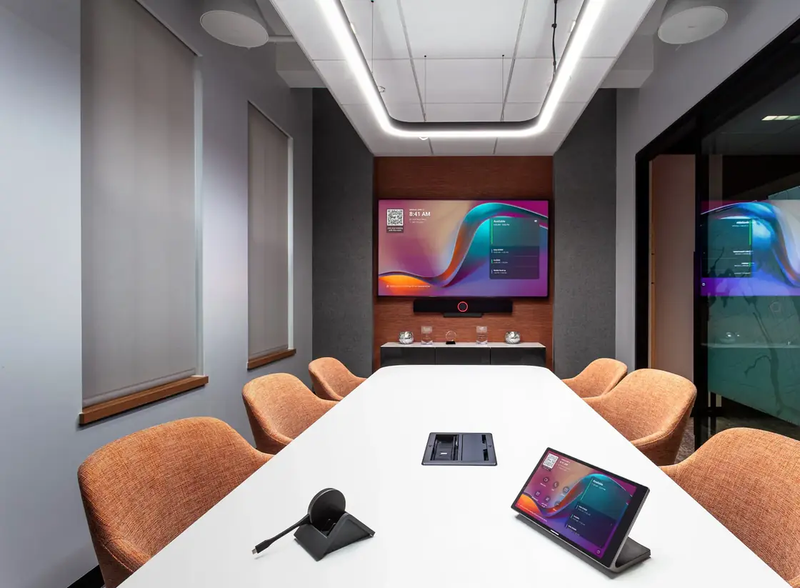 Sala de reuniones con videoconferencia, parlantes de techo y panel de control en la mesa